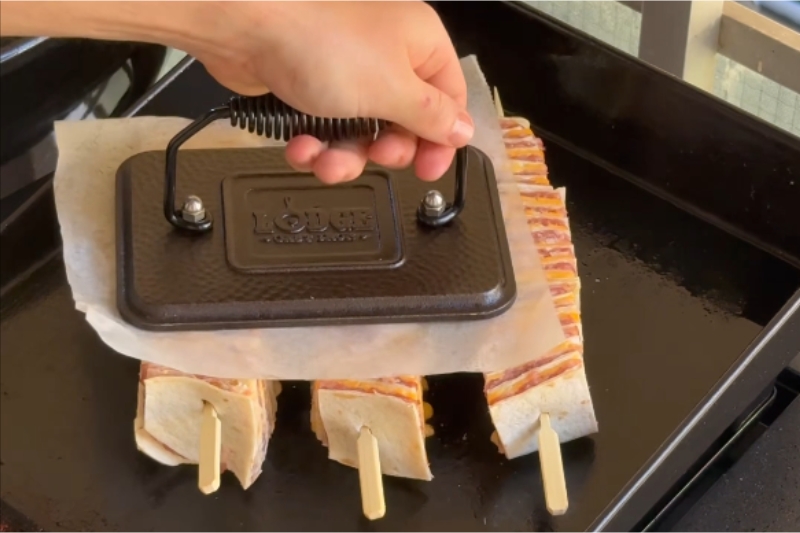 Burger σουβλάκι smash με τορτίγια και bacon πιέζεται στην Plancha με βαρίδι ψησίματος
